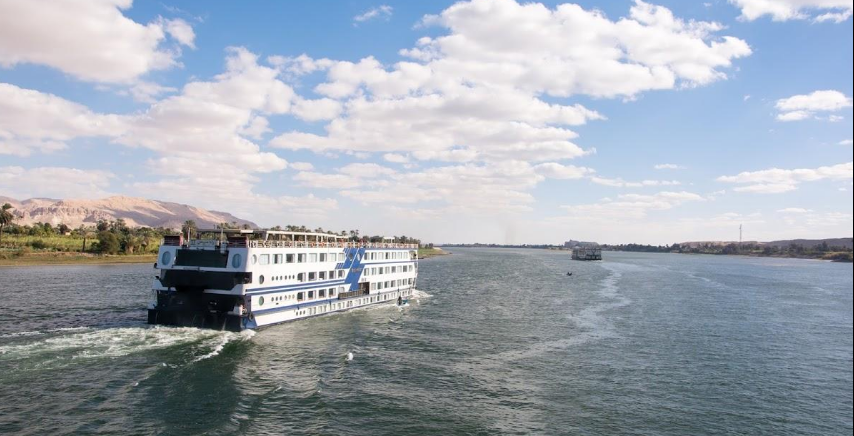 A group of international travellers relaxing on the upper deck of a Nile cruise ship, enjoying the river scenery and taking photographs.