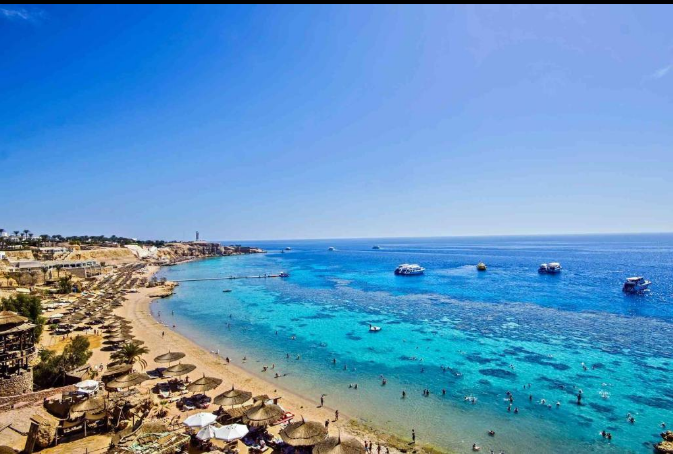 Naama Bay with sandy beach, clear Red Sea water and surrounding mountains.