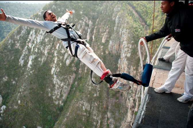 An adventurer jumping from a high bridge surrounded by spectacular scenery.